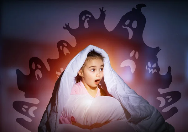 Excited girl hiding under blanket from imaginary ghosts. Scared kid sitting in his bed at home. Little girl afraid of fantasy monsters. Covered child in pajamas not sleep at night. Halloween holiday.
