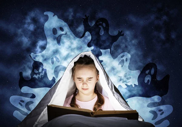 毛布の下で本を読んで怖い子供 自宅でベッドに寝そべって目を閉じた少女を恐れている 子供は怖い話を読む パジャマ姿の少女と想像上の幽霊オープンブックから輝く明るい光 — ストック写真