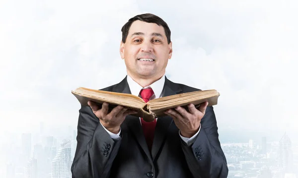 Happy businessman holding open old book. Smiling man in business suit standing on downtown background. Lawyer holding big legal regulation book. Professional business accounting and consulting
