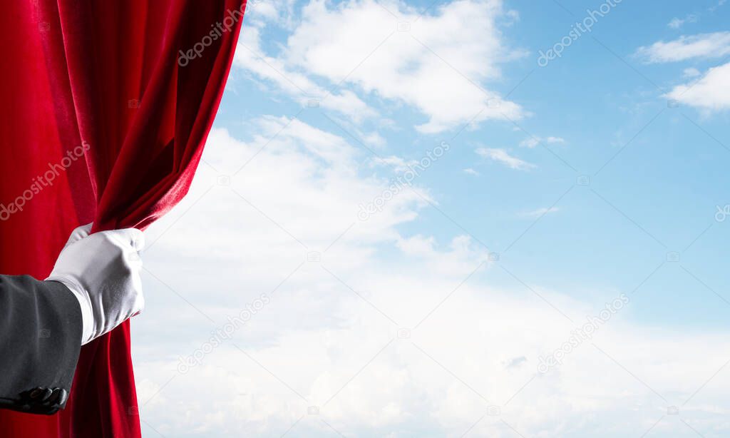 Human hand in glove opens red velvet curtain on blue sky background