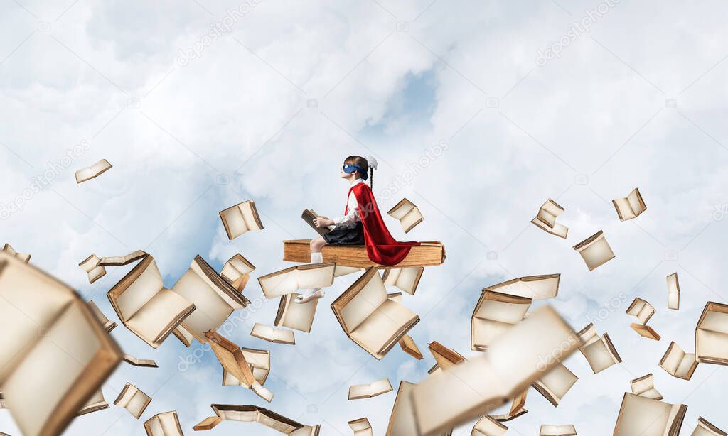 Little child in mask and cape floating on book in sky and reading