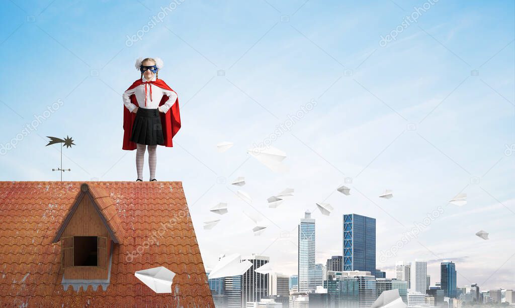 Young girl in superhero costume standing on house brick roof. Mixed media