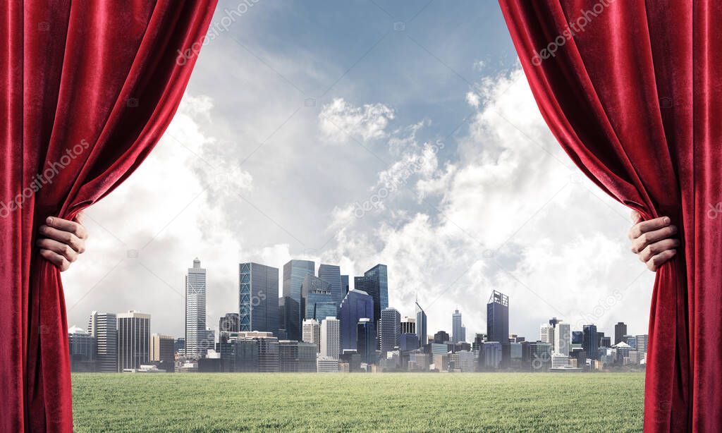 Human hand opens red velvet curtain to cityscape and green meadow
