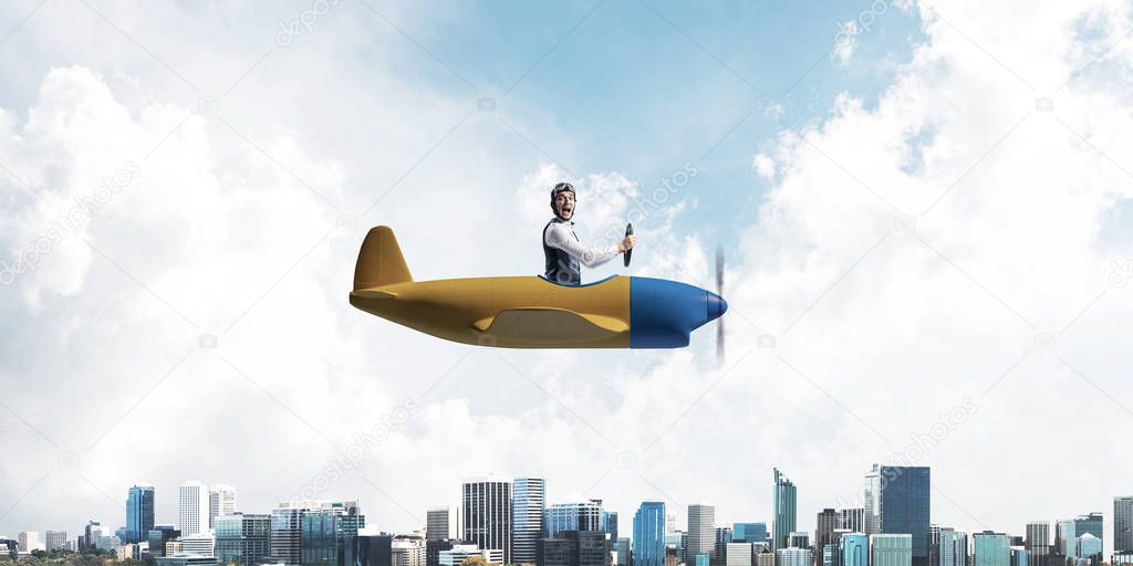 Businessman in aviator hat and goggles driving propeller plane above downtown with high modern buildings. Funny man having fun in small airplane. Blue sky landscape with clouds on background