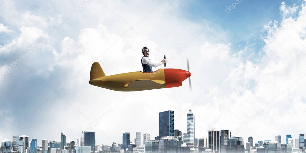 Business direction and motivation concept with pilot sitting in cabin of small airplane. Funny man in aviator hat and goggles driving propeller plane above city. Modern metropolis with high buildings