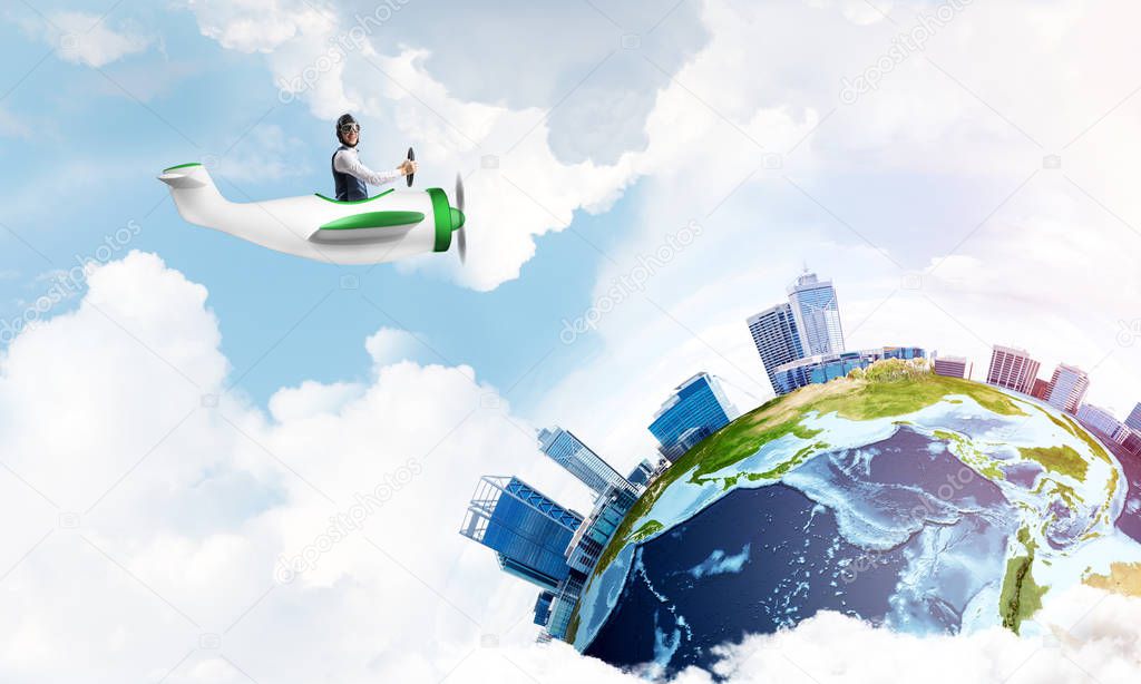 Businessman in aviator leather hat driving propeller plane. Traveling around the world by airplane. Funny man flying in small airplane in blue sky with clouds. Earth planet with modern cityscape.