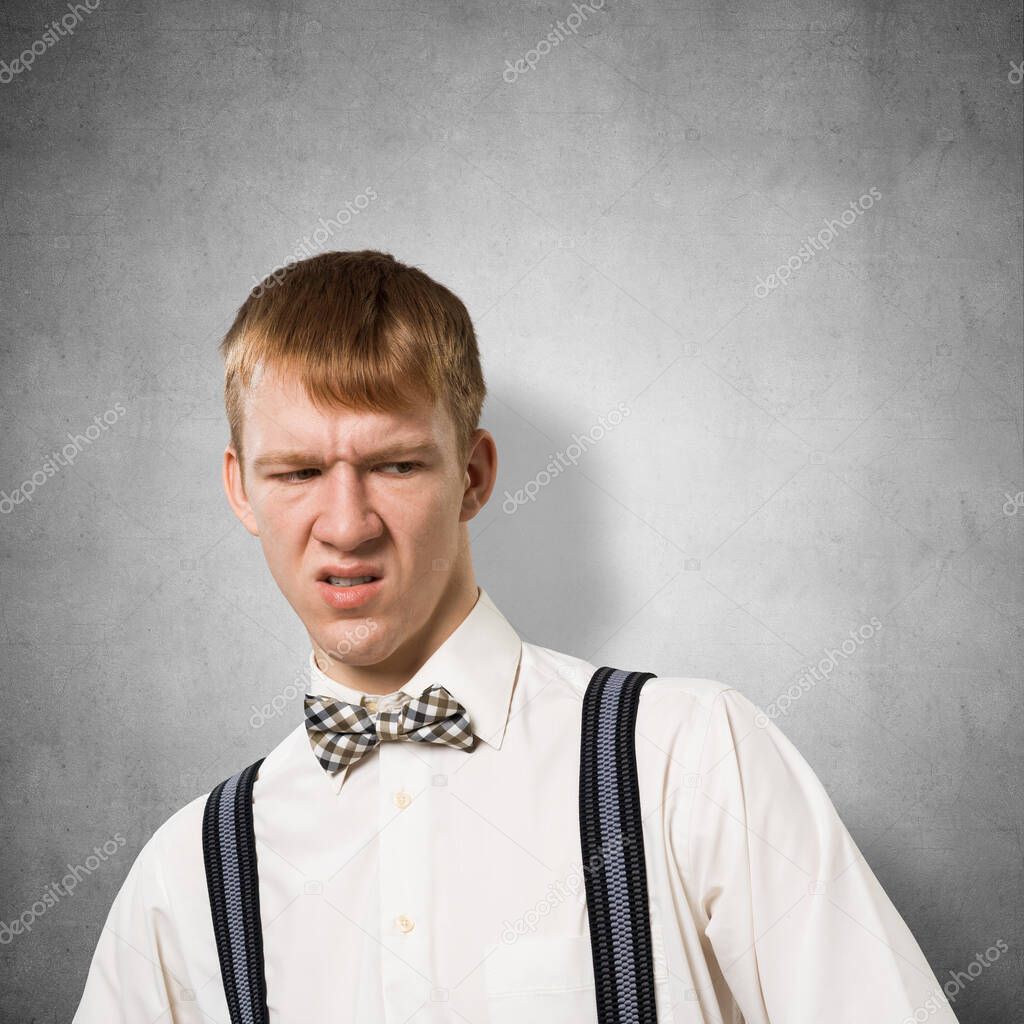 Ugh, how disgusting. Displeased redhead hipster. Emotional boy has dissatisfied facial expression as sees something abominable or detestable. Portrait of guy wears white shirt, bow tie and suspenders