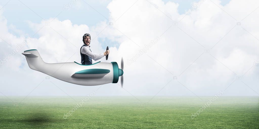 Happy aviator driving propeller plane. Emotional pilot in leather helmet looking in camera. Man in airplane flying low above green meadow. Nature panorama with green grass and cloudy sky in summer day