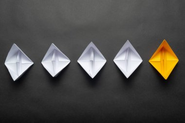 Siyah arka plan üzerinde kağıt gemi sırası. Yaratıcı yenilik ve liderlik iş kavramı. Düz beyaz tekne grubunda sarı origami tekne yatıyordu. Kopyalama alanı ile sosyal pazarlama düzeni.