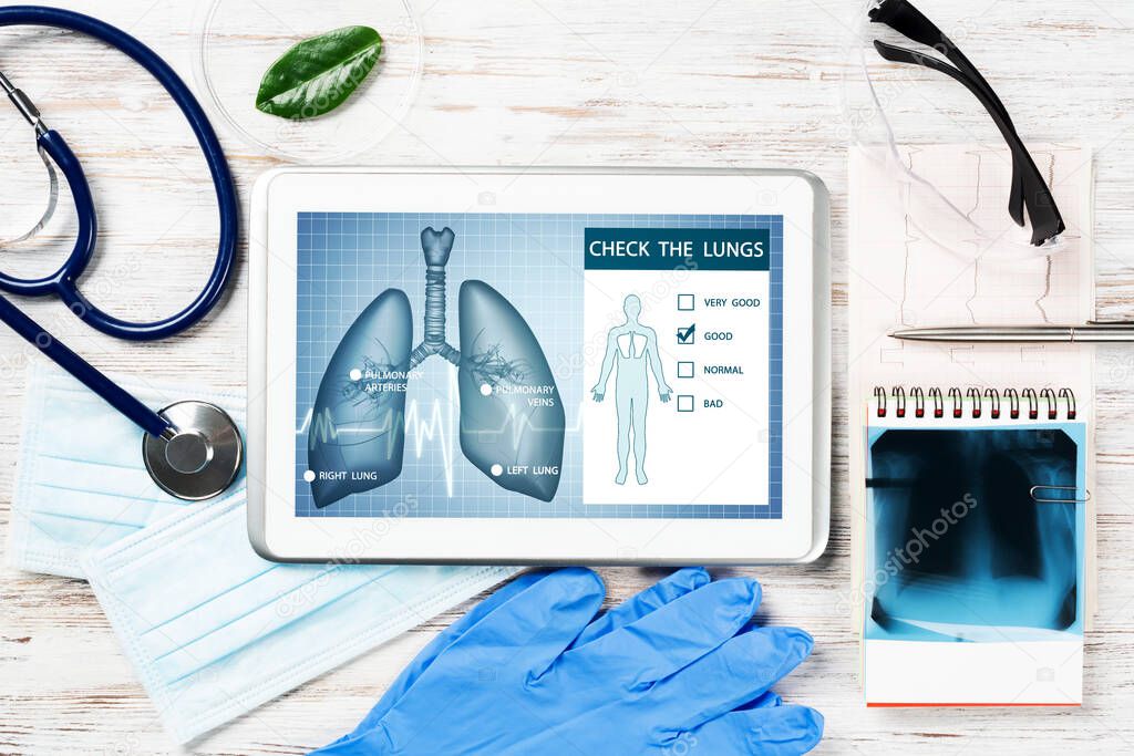 Medical diagnostics in modern pulmonology. Tablet computer with medical application interface on screen. Top view x-ray image, stethoscope and cardiogram on desk. Digital tuberculosis screening test
