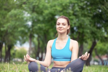 Kız nilüferde meditasyon yapıyor yeşil çimlerde poz veriyor. Yaz parkında yoga pratiği yapıyorum. Huzurlu genç bir kadının portresi. Yaz günü dışarıda antrenman ve meditasyon. Sağlıklı yaşam tarzı ve rahatlama.