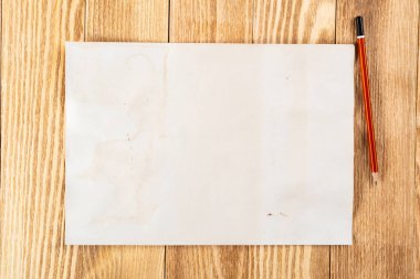 Tahta masanın üzerinde duran bir yaprak kağıt. Boş beyaz a4 formatlı kalem kağıdı. Dokulu doğal ahşap arka plan. Tasarım için klasik kopyalama alanı. İş planlaması ve fikir üretimi.