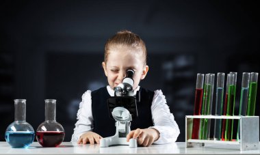 Sınıfta mikroskoba bakan küçük bir bilim adamı. Modern okulda araştırma ve eğitim. Cam mataraları ve test tüpleri olan kimya laboratuvarı. Öğrenci kız kimya dersinde deney yapıyor.