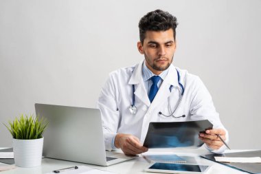 Yakışıklı genç doktor röntgen taramasına bakıyor. Steteskoplu beyaz önlüklü bir doktor masada dizüstü bilgisayarla oturuyor. Profesyonel tıbbi teşhis ve hastanede tedavi. Sağlık hizmetleri
