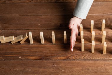 İş kadını, tahta domino taşlarını düşürerek domino etkisini engelliyor. Operatif iş çözümü, strateji ve başarılı müdahale. İş yardımı, koruma ve krizin önlenmesi