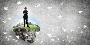 Yeşil yüzen adada beton zemine karşı duran kendine güvenen zarif iş adamı.