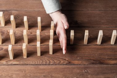 İş kadını domino etkisini engelliyor. İş yardımı, risk yönetimi ve istikrar durumu. Masada tahta bloklar varken işlem konseptine müdahale. Ekonomik çöküşten korunma.