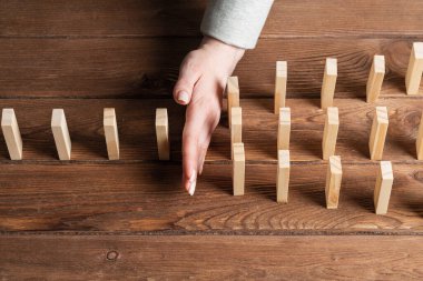 İş kadını domino etkisini engelliyor. İş yardımı, risk yönetimi ve istikrar durumu. Masada tahta bloklar varken işlem konseptine müdahale. Ekonomik çöküşten korunma.