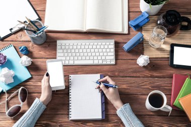 Ofis masasında akıllı telefon kullanan bir iş kadını. Çevrimiçi iş uygulaması kavramı. Kadın eli ve klavyesi olan düz bir ofis işyeri. İş için dijital teknoloji ve mobil uygulama.