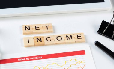 Tahta küplerde harflerle net gelir kavramı. Malzemelerle dolu ofis hayatı. Tablet bilgisayarlı ve analitik raporlu düz beyaz yüzey. Finansal başarı ve yatırım.