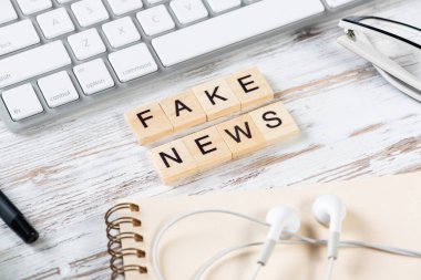 Küplerdeki harflerle sahte haber kavramı. Bilgisayar klavyesi, kulaklığı ve not defteri olan eski tip tahta bir masa. Medya teknolojisini yanlış bilgilendirme. Gazeteci işyerinin hayatı.