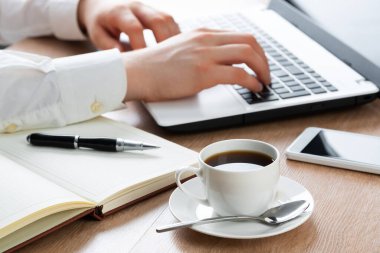 Ofisteki dizüstü bilgisayarda çalışan bir iş adamı. Dizüstü bilgisayarda daktilo eden erkek ellerinin yakın çekimi. İş yerinde iş adamı, elinde akıllı telefon ve bir fincan kahveyle. İş ve dijital teknoloji.