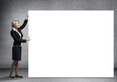 Takım elbiseli güzel bir kadın büyük beyaz pankartın yanında duruyor. İleti için kopyalama alanı olan boş bir beyaz tahta şablonu. İş kadını sunum ve tanıtım gibi bir şey. Ticari reklamcılık ve pazarlama.