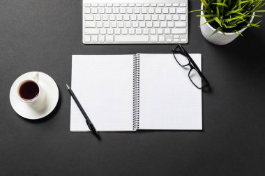 Bir fincan kahveli modern ofis işyeri manzarası. Düz siyah yüzey bilgisayar klavyesi ve açık not defteri ile yatıyordu. Üst düzey çalışma alanı ve serbest çalışma. Dijital teknoloji ve hareketlilik.