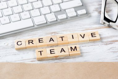 Küp üzerinde harflerle yaratıcı takım konsepti. Malzemelerle dolu ofis çalışma alanı. Bilgisayar klavyesi ve not defteri olan eski tip tahta bir masa. Takım çalışması ve iş birliği.