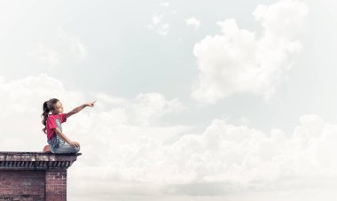 Üstte oturan ve bir şeyi işaret eden sevimli bir kız.