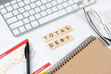 Küpler üzerindeki harflerle birlikte toplam borç kavramı. Malzemelerle dolu ofis hayatı. Düz beyaz yüzey, not defteri, bilgisayar klavyesi ve mali raporuyla yatıyordu. Sermaye yönetimi ve bankacılık.