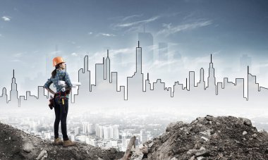 Sert şapkalı kadın mühendis elinde teknik planlarla ayakta duruyor. İş kıyafetleri içindeki kadın mimarın arka planı gökdelenleri yüksek modern şehir hayalleri kuruyor. Şehir merkezi proje tasarımı ve inşaatı