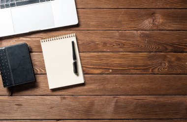 Malzemelerle dolu modern ofis çalışma alanı. Düz tahta masa, dizüstü bilgisayarı, günlüğü ve kalemi vardı. Zaman yönetimi ve gündüz planlama. Şirket iş konsepti.