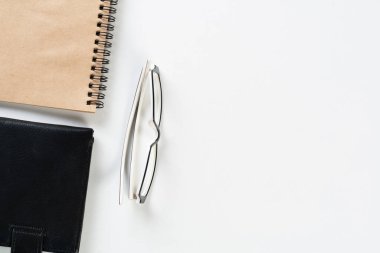 Malzemelerle dolu modern ofis çalışma alanı. Siyah deri cüzdanı ve sarmal not defteriyle bembeyaz bir masa. Muhasebe ve bankacılık hizmeti. Kopya alanı ile finans ve yatırım kavramı