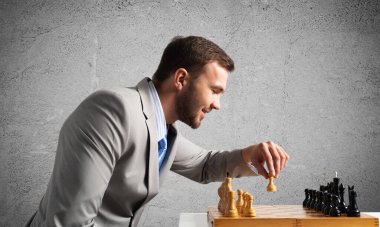 Satranç oynayan konsantre bir iş adamı. Başarılı yönetim ve liderlik kavramı. Takım elbiseli, satranç masasında oturan kendinden emin genç bir adam. Operasyon taktikleri ve strateji planlaması