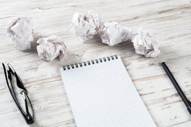 Ofiste buruşuk kağıt topları olan üst düzey tasarımcı işyeri. Krizden yaratıcı ilhama. Boş defterli düz tahta bir masa. Fikir üretimi ve beyin fırtınası. Harika bir çözüm ara