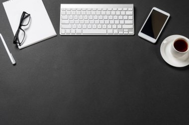 Dijital aletlerle ofis işyerinin en üst görüntüsü. Düz siyah yüzey, bilgisayar klavyesi, akıllı telefon ve not defteriyle yatıyordu. Üst düzey çalışma alanı ve serbest çalışma. Dijital teknoloji ve hareketlilik.