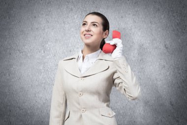 Elinde retro kırmızı telefon tutan gülümseyen genç bir kadın. Beyaz takım elbiseli çağrı merkezi operatörü elinde sabit hatlı telefonla poz veriyor. Telepazarlama konsepti. İş yardımı ve danışma.