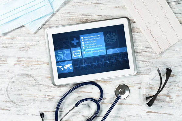 Modern social health insurance program. Tablet computer with healthcare application interface on screen. Top view doctor workplace with stethoscope and cardiogram. Digital healthcare technologies.
