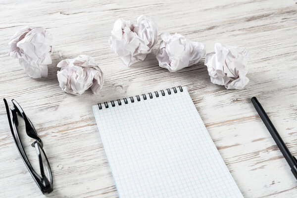 Top view designer workplace in office with crumpled paper balls. Crisis to creative inspiration. Flat lay wooden desk with blank notebook. Idea generation and brainstorming. Search for great solution