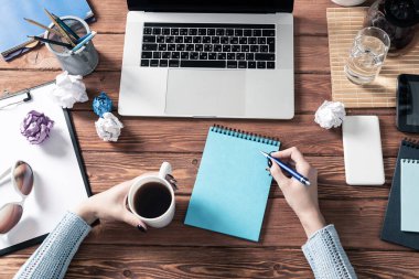 Masasında kalemle deftere yazan bir kadın. Çevrimiçi iş eğitimi. Düz ofis işyeri, kadın eli ve dizüstü bilgisayarı. Dijital teknoloji ve ortak çalışma alanı. Kadın gazeteci not alıyor