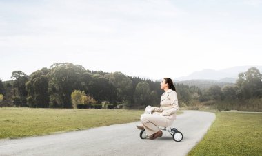 Güzel beyaz kadın asfalt yolda çocuk bisikleti sürüyor. Beyaz takım elbiseli genç bir işçi dışarıda bisiklet sürüyor. Profesyonel kariyer başlangıcı. Kadın bisikletçiyle başlangıç düzeyi konsepti.