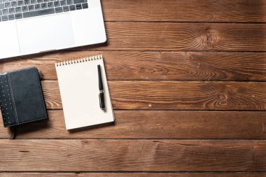 Malzemelerle dolu modern ofis çalışma alanı. Düz tahta masa, dizüstü bilgisayarı, günlüğü ve kalemi vardı. Zaman yönetimi ve gündüz planlama. Şirket iş konsepti.