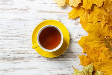 Düz sonbahar kompozisyonu, bir fincan siyah çay ve sarı sonbahar yapraklarıyla yatıyordu. Çay molası zamanı. Sıcak içecek, parlak yapraklı eski ahşap masanın üzerinde yatıyor. Sabahki çay seremonisi hayatı.