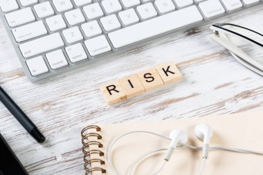 Küpler üzerindeki harflerle risk yönetimi kavramı. Malzemelerle dolu ofis hayatı. Bilgisayar klavyesi, kulaklığı ve not defteri olan eski tip tahta bir masa. Uyumlu organizasyon.