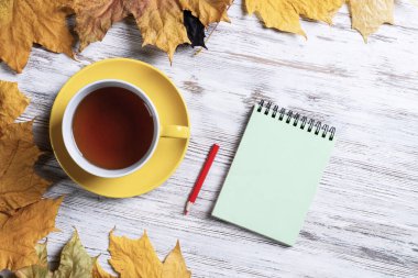 Düz sonbahar kompozisyonu, bir fincan siyah çay ve sarı sonbahar yapraklarıyla yatıyordu. Çay molası zamanı. Sıcak içecek ve kalemle dolu bir hayat eski ahşap masa üzerinde parlak yapraklarla uzanır..