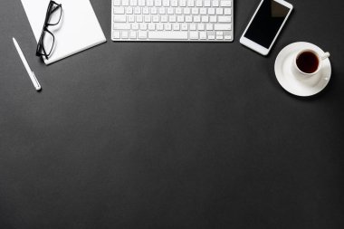 Dijital aletlerle ofis işyerinin en üst görüntüsü. Düz siyah yüzey, bilgisayar klavyesi, akıllı telefon ve not defteriyle yatıyordu. Üst düzey çalışma alanı ve serbest çalışma. Dijital teknoloji ve hareketlilik.