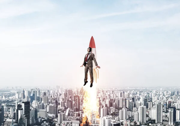 Business person in aviator hat flying on rocket. Progress and innovation technology. Corporate businessman flying with jetpack rocket in blue sky above modern city. Leadership motivation concept.