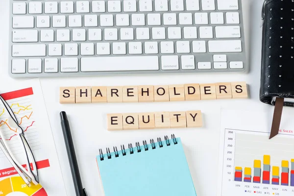 Shareholders equity concept with letters on cubes. Still life of office workplace with supplies. Flat lay white surface with computer keyboard and analytic report. Financial capital and investment.