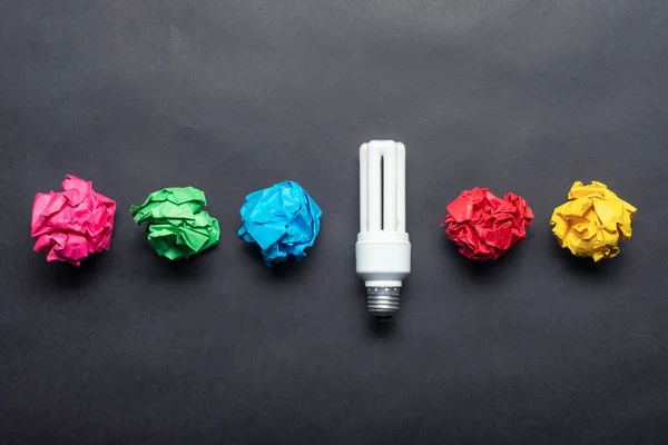 Fluorescent lamp and crumpled colorful paper balls on black background. Successful solution of problem. Idea generation and brainstorming motivation. Great idea among failing ideas metaphor.